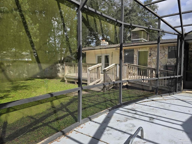 view of front of house featuring glass enclosure, stone siding, a front lawn, and a deck