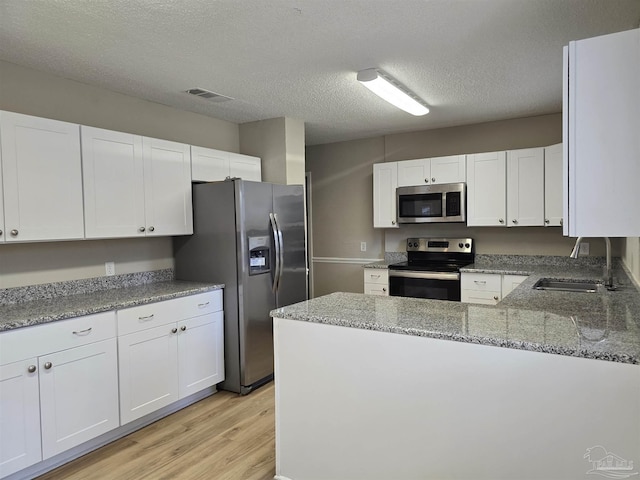 kitchen featuring light stone counters, stainless steel appliances, visible vents, white cabinetry, and a sink