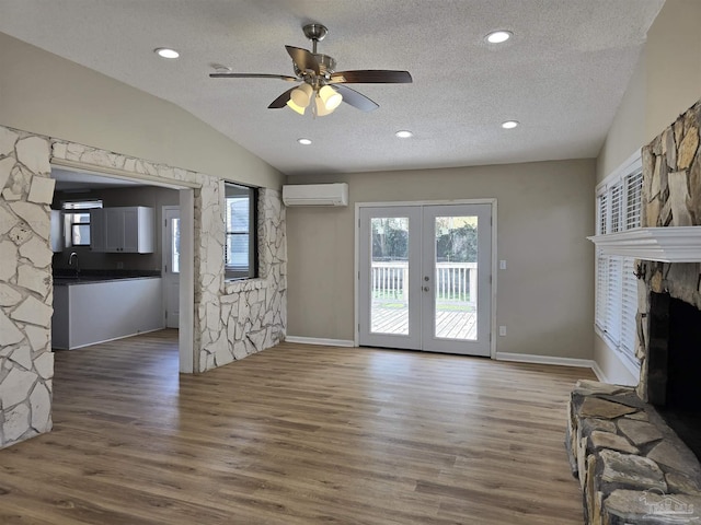 unfurnished living room with a textured ceiling, wood finished floors, vaulted ceiling, french doors, and a wall mounted air conditioner