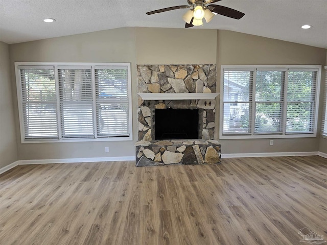 living area featuring lofted ceiling, a healthy amount of sunlight, and a stone fireplace