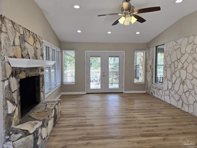 unfurnished living room with lofted ceiling, a stone fireplace, wood finished floors, french doors, and a wealth of natural light