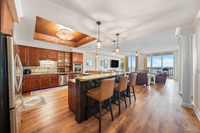 kitchen with decorative columns, appliances with stainless steel finishes, a breakfast bar, and a tray ceiling