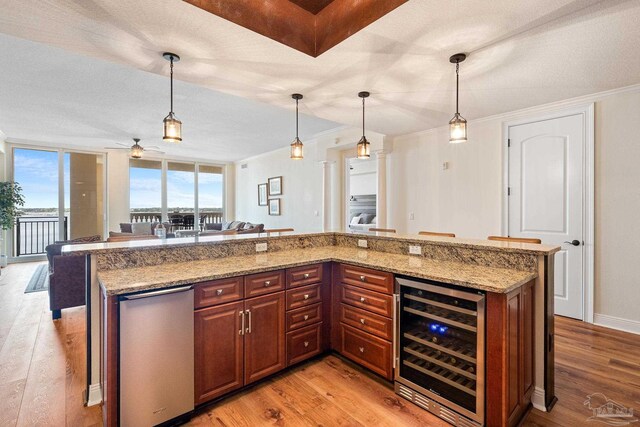 kitchen featuring light stone countertops, pendant lighting, beverage cooler, and light hardwood / wood-style flooring