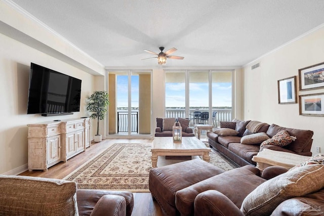 living room with a textured ceiling, light wood-type flooring, ornamental molding, expansive windows, and ceiling fan