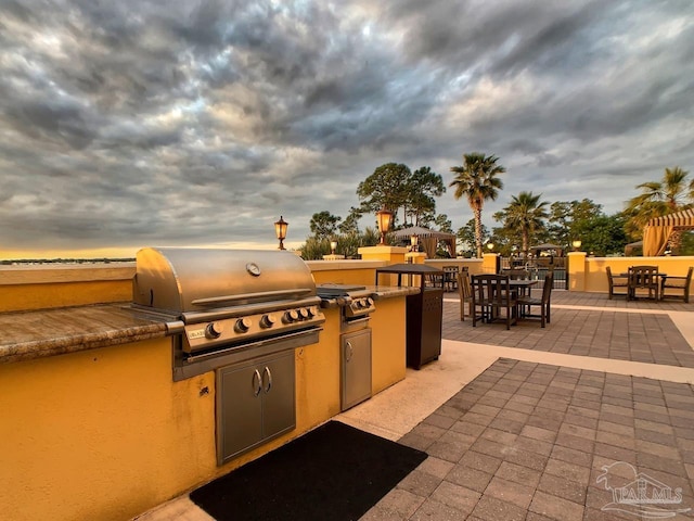 patio terrace at dusk featuring grilling area and exterior kitchen