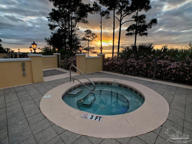 pool at dusk with a hot tub and a patio