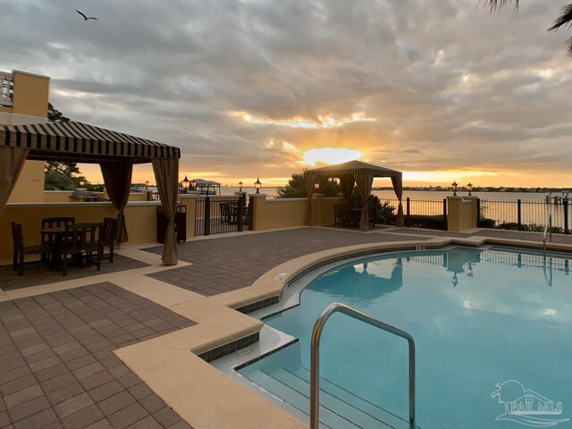 pool at dusk featuring a gazebo and a patio