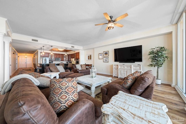 living room with light hardwood / wood-style floors, decorative columns, and ceiling fan