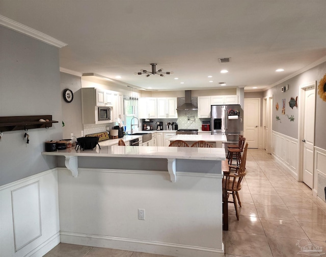 kitchen with wall chimney exhaust hood, a kitchen breakfast bar, kitchen peninsula, stainless steel appliances, and white cabinetry