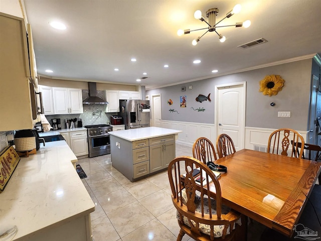 kitchen featuring gray cabinetry, wall chimney range hood, a center island, stainless steel appliances, and ornamental molding