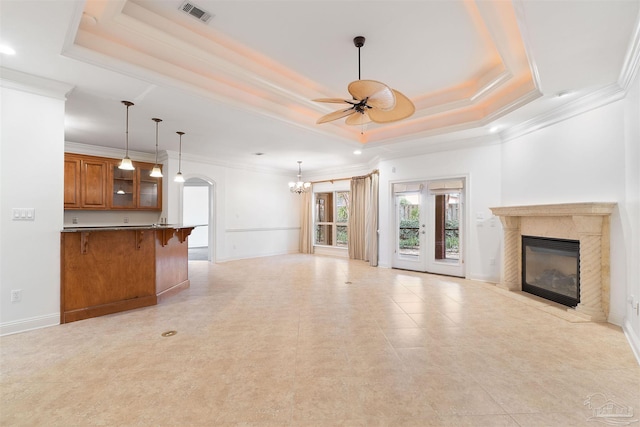 unfurnished living room featuring crown molding, a raised ceiling, a premium fireplace, and ceiling fan with notable chandelier