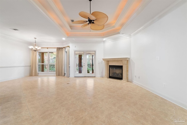 unfurnished living room featuring ornamental molding, a high end fireplace, a tray ceiling, and ceiling fan with notable chandelier