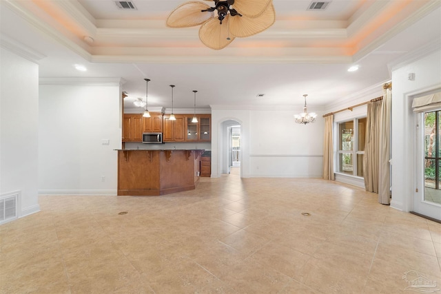 kitchen featuring a breakfast bar area, ornamental molding, a tray ceiling, and ceiling fan with notable chandelier