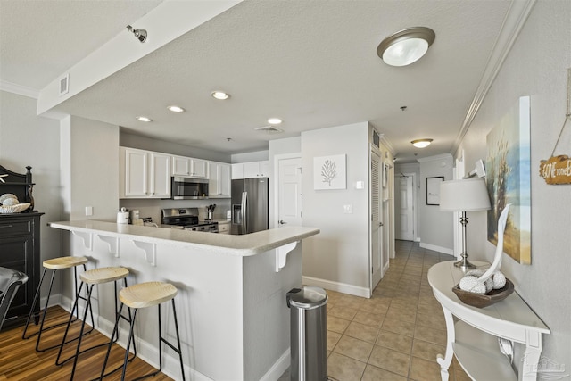 kitchen with white cabinets, kitchen peninsula, appliances with stainless steel finishes, and a breakfast bar