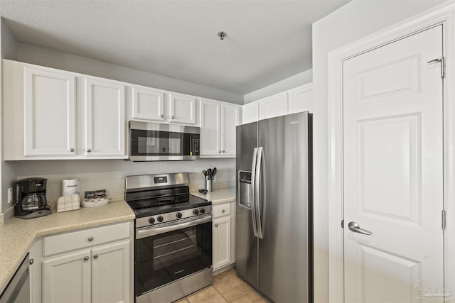 kitchen with light tile patterned floors, a textured ceiling, stainless steel appliances, and white cabinetry