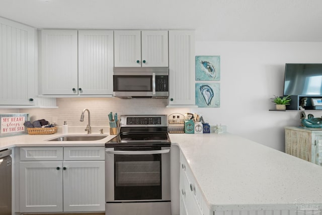 kitchen with light countertops, a peninsula, tasteful backsplash, appliances with stainless steel finishes, and a sink