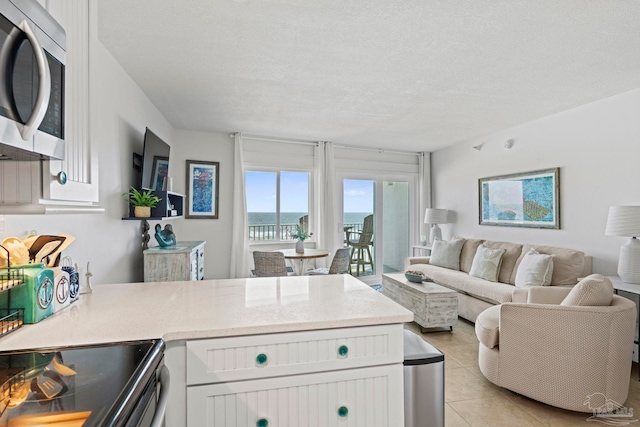 kitchen featuring white cabinetry, a peninsula, light tile patterned floors, and stainless steel microwave