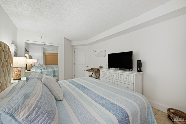 bedroom featuring baseboards, light tile patterned floors, and a textured ceiling