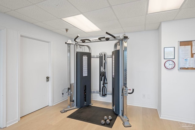 exercise room with a paneled ceiling, baseboards, and wood finished floors