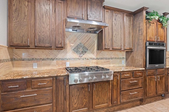 6781 Generals Ln, Pace, FL 32571 - kitchen with under cabinet range hood, appliances with stainless steel finishes, tasteful backsplash, light stone countertops, and light wood finished floors