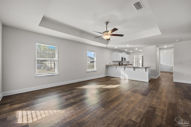 unfurnished living room with dark wood-type flooring, a tray ceiling, and ceiling fan