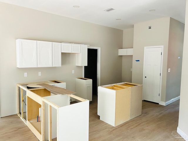 kitchen with white cabinets, visible vents, light wood-style flooring, and a center island