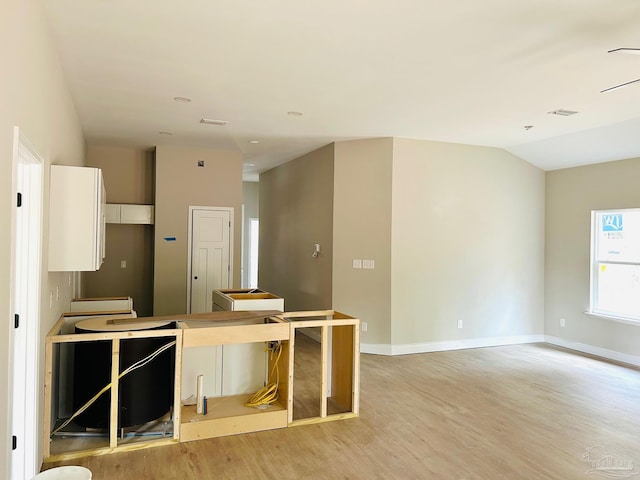 kitchen with lofted ceiling, visible vents, white cabinetry, light wood-type flooring, and baseboards