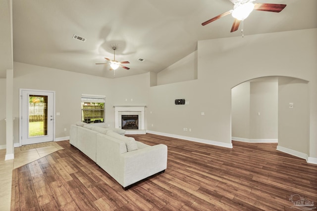 living room featuring a ceiling fan, arched walkways, dark wood-style flooring, a fireplace with raised hearth, and baseboards