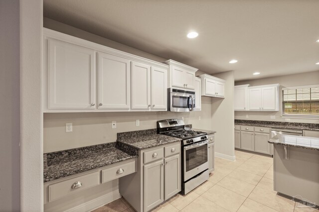 kitchen with appliances with stainless steel finishes, dark stone counters, white cabinetry, light tile patterned flooring, and recessed lighting
