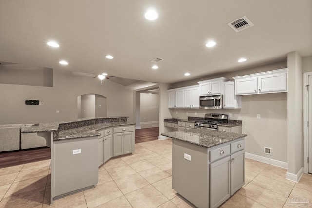 kitchen featuring stainless steel appliances, a kitchen island, arched walkways, recessed lighting, and white cabinetry