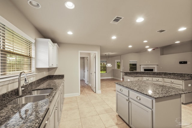 kitchen with a sink, a center island, baseboards, light tile patterned floors, and white cabinetry