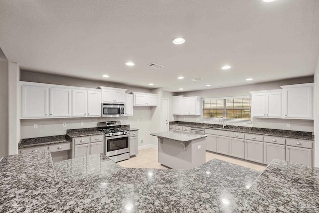 kitchen featuring appliances with stainless steel finishes, a sink, light tile patterned flooring, white cabinetry, and dark stone counters