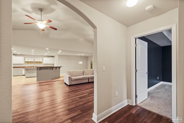 hallway with vaulted ceiling, dark wood-style flooring, arched walkways, baseboards, and recessed lighting