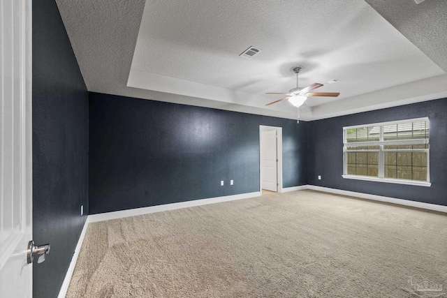 carpeted empty room featuring a tray ceiling, ceiling fan, a textured ceiling, and baseboards