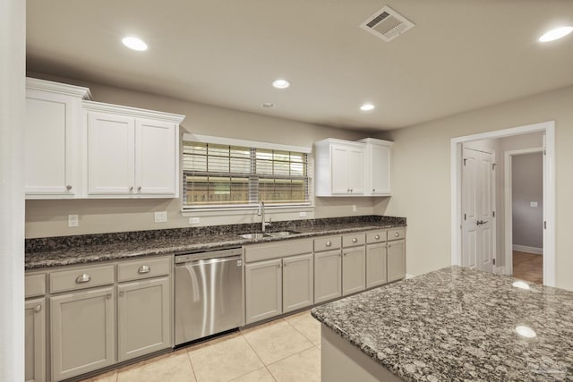 kitchen with stainless steel dishwasher, a sink, dark stone counters, recessed lighting, and light tile patterned flooring