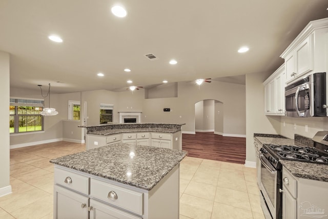 kitchen with appliances with stainless steel finishes, a center island, open floor plan, arched walkways, and light tile patterned flooring