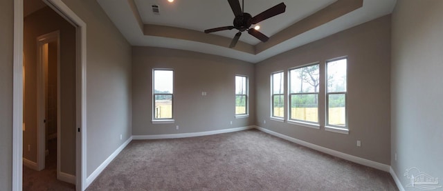 carpeted empty room with baseboards, visible vents, ceiling fan, and a raised ceiling