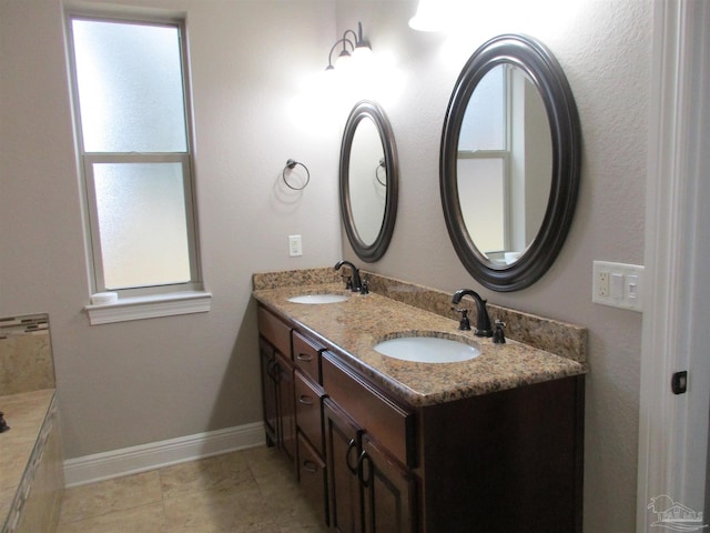 bathroom with baseboards, double vanity, and a sink