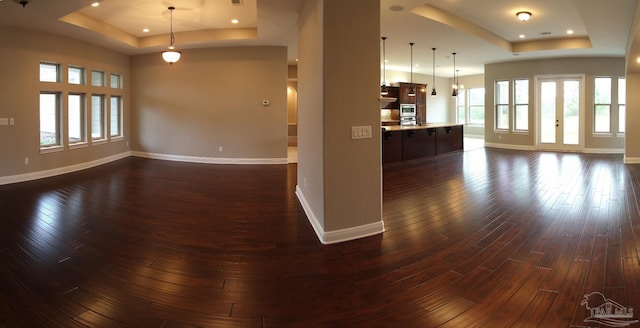 unfurnished living room featuring dark wood-style floors, recessed lighting, baseboards, and a raised ceiling