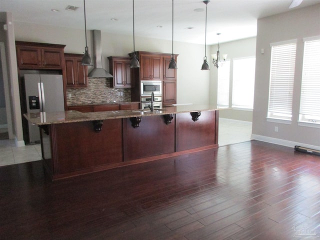 kitchen featuring stainless steel appliances, a breakfast bar, backsplash, a sink, and wall chimney range hood