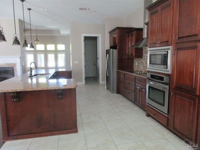 kitchen featuring wall chimney exhaust hood, stainless steel appliances, tasteful backsplash, a sink, and light stone counters