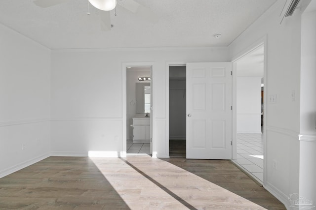 unfurnished bedroom with a textured ceiling, ensuite bath, dark wood-type flooring, and ceiling fan