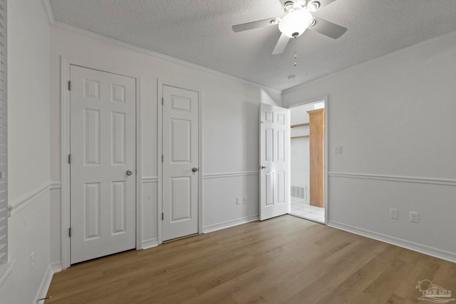 unfurnished bedroom featuring a textured ceiling, light hardwood / wood-style flooring, ornamental molding, and ceiling fan