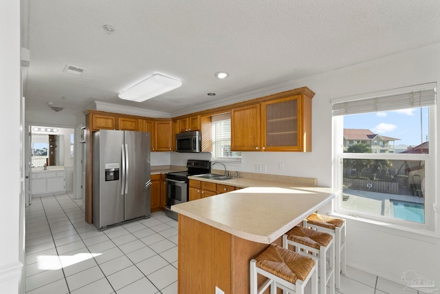 kitchen with kitchen peninsula, a textured ceiling, light tile patterned floors, a breakfast bar, and appliances with stainless steel finishes