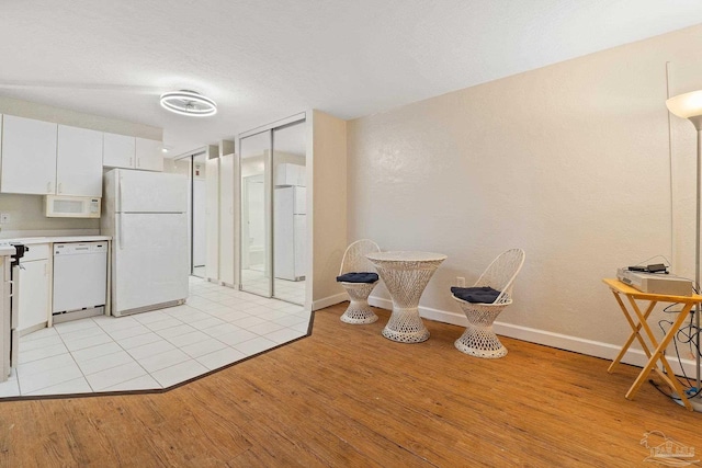 kitchen with white cabinetry, white appliances, and light hardwood / wood-style floors