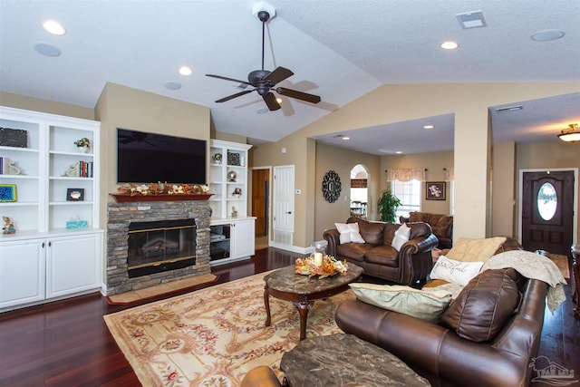 living area featuring dark wood finished floors, a ceiling fan, vaulted ceiling, a stone fireplace, and a textured ceiling