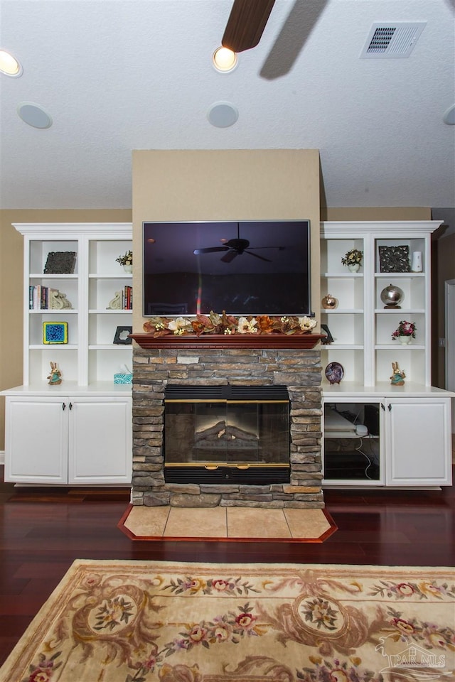 living area featuring a ceiling fan, dark wood finished floors, visible vents, and a fireplace