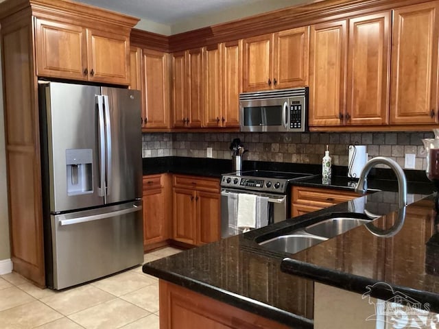 kitchen with light tile patterned floors, decorative backsplash, appliances with stainless steel finishes, brown cabinetry, and a sink