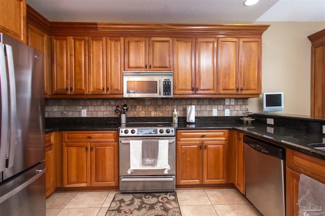 kitchen with brown cabinetry, dark stone counters, and stainless steel appliances