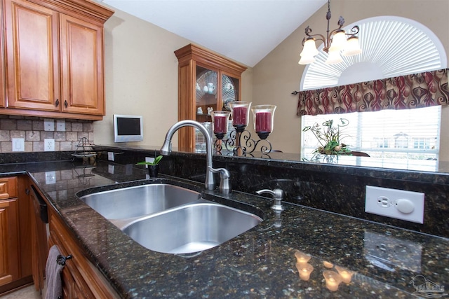 kitchen with brown cabinetry, lofted ceiling, dark stone countertops, decorative light fixtures, and a sink